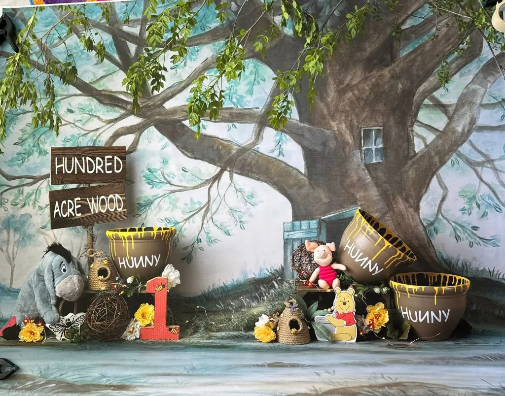 Woodland first-birthday photography backdrop with honey pots and a number one