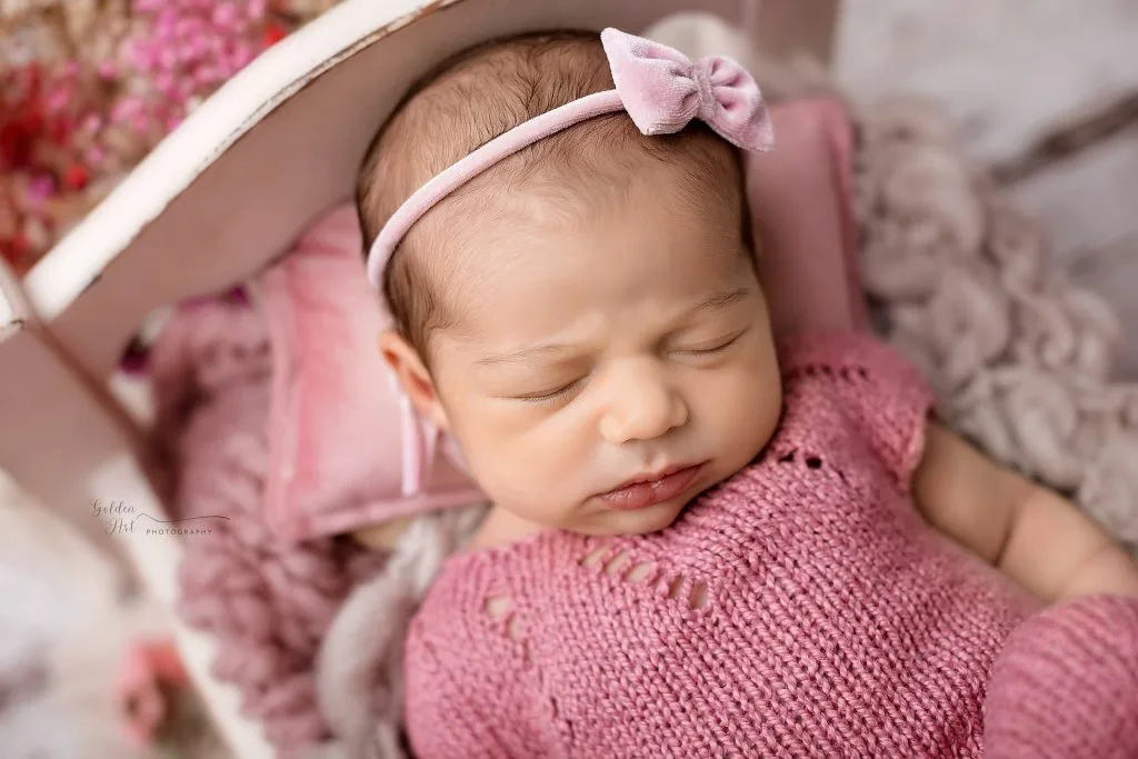 Close-up newborn portrait with a pink bow and knitted wrap
